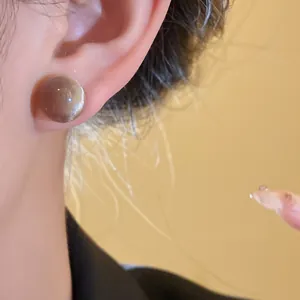 Detail view of a round translucent resin stud earring with a minimalist brown finish