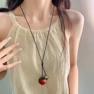 Close-up of a Bohemian style ceramic red persimmon pendant necklace worn by a female model