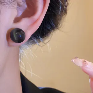 Close-up view of a minimalist dark round resin stud earring with silver needle on ear