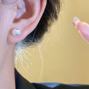 Close-up detail showing a minimalist round white resin pearl stud earring worn on an ear.