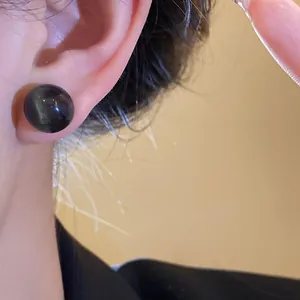 Close-up detail of a minimalist black resin pearl stud earring on an Asian model's ear
