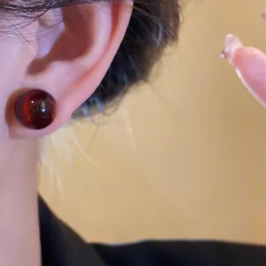 Close-up of a minimalist round dark red resin stud earring worn on an ear