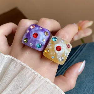 Close-up of chunky marbled resin rings with multi-colored inlaid rhinestones.