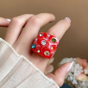 Macro view of a vibrant red chunky resin ring with colorful rhinestones on a hand.