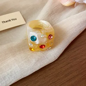 Close-up of a chunky beige resin ring with colorful rhinestones on soft beige fabric