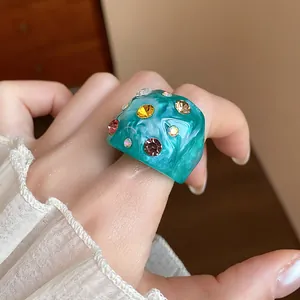 Close-up of a teal wrinkled resin ring with colorful rhinestones on a model's finger