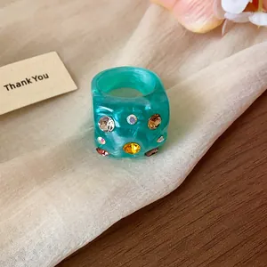Close-up of a turquoise resin ring featuring colorful rhinestones and a unique crumpled texture
