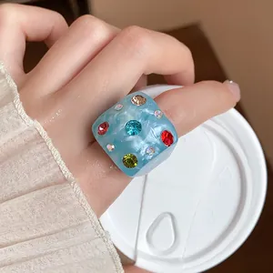 Detail view of a blue marble-textured cube ring with colorful rhinestones on finger.
