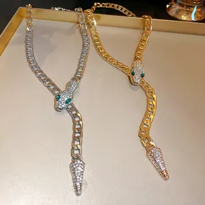 Detail view of gold and silver snake-shaped necklaces with paved stones and green eyes