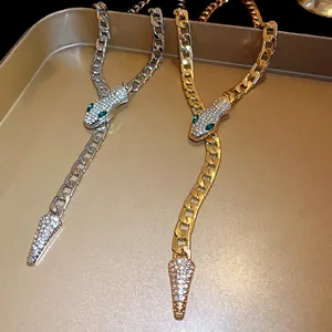 Close-up of gold and silver snake necklaces with rhinestones and green eyes on a tray.