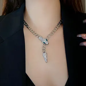 Close-up detail of a sparkling silver snake head necklace with green eyes on a model