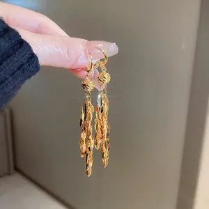 Detailed macro view of gold leaf sequin tassel dangle earrings held by hand.