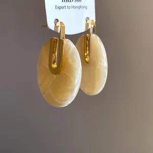 Dettaglio di eleganti orecchini in acetato marmorizzato crema con placcatura oro 18K