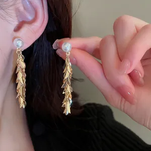 Detailed close-up of elegant golden leaf sequin tassel earrings with pearl studs