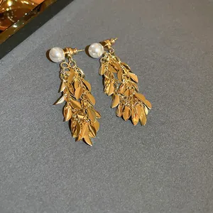 Close-up view of golden leaf tassel earrings featuring pearl studs and metallic sequins