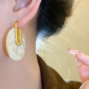 Primo piano dettagliato di orecchini tondi in acetato placcato oro 18K indossati sull'orecchio