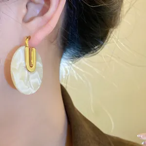 Dettaglio ravvicinato di un orecchino dorato con disco in acetato bianco marmorizzato all'orecchio.