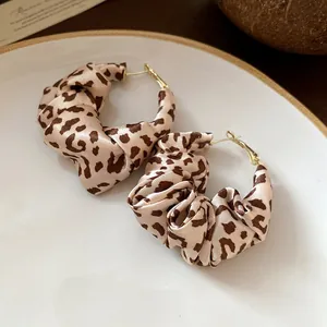 Close-up of leopard print fabric wrapped hoop earrings with an elegant twisted texture