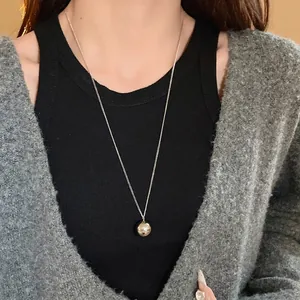 Minimalist silver-tone round ball pendant necklace worn with a grey cardigan.