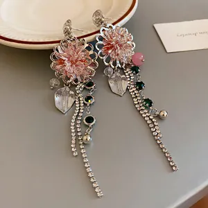 Close-up of floral crystal earrings with rhinestone tassels and emerald green accents.