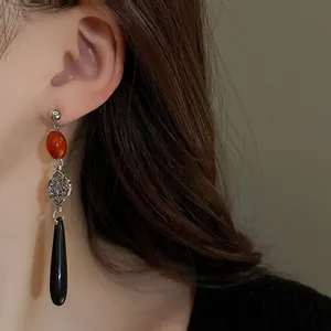 Dettaglio degli orecchini pendenti in stile cinese con una perla rossa e un pendente