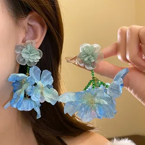 Dettaglio di orecchini a fiore in chiffon blu con ago d'argento sull'orecchio