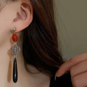 Dettaglio di orecchini pendenti in stile cinese con perla rossa e ciondolo a goccia nero