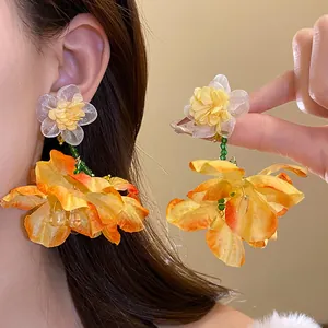 Vista dettagliata di orecchini a goccia in chiffon giallo e arancione sull'orecchio di una modella