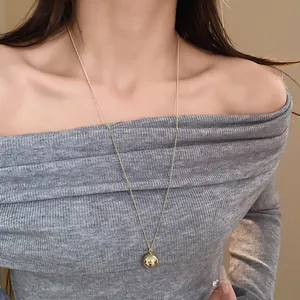 Close-up of a minimalist gold ball pendant long necklace worn over a grey sweater.