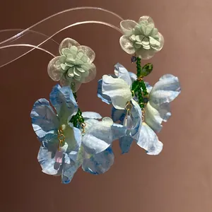 Dettaglio di eleganti orecchini a fiore in chiffon con petali blu e perline verdi
