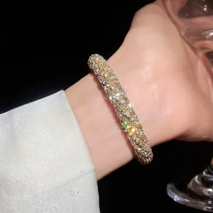 Close-up of a sparkling gold-tone bangle encrusted with shimmering rhinestones on a wrist.