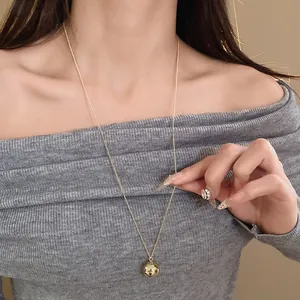 Close-up of a minimalist golden spherical pendant necklace worn with a grey sweater