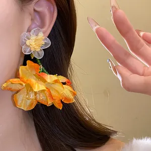 Primo piano di orecchini pendenti a fiore in chiffon arancione, stile vacanza elegante.