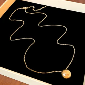 Close-up detail of elegant gold sphere pendant necklace displayed on a black background tray