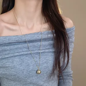 Close-up of a minimalist gold spherical pendant necklace on a grey ribbed sweater