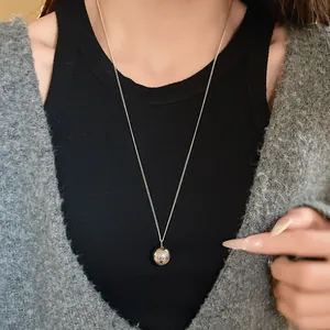 Close-up view of a minimalist silver ball pendant necklace styled with a grey cardigan