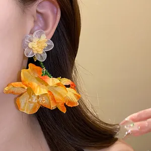 Primo piano di eleganti orecchini a goccia in chiffon arancione indossati sull'orecchio del modello