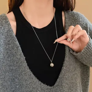 Close-up of a minimalist silver round pendant necklace worn over a stylish grey cardigan