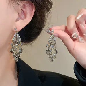 Detail view of luxury zircon tassel earrings with grey teardrop glass beads on model's ear