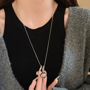 Close-up detail of a minimalist silver round pendant necklace on a grey sweater