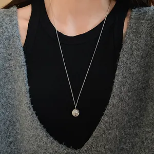 Close-up of minimalist silver round ball pendant necklace worn on black sweater
