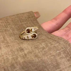 Dettaglio macro di un anello aperto dorato con pietre marroni e zirconi bianchi lucidi