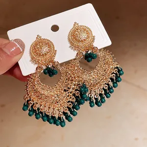 Close-up of vintage gold-tone ethnic chandelier earrings featuring emerald green bead tassels.