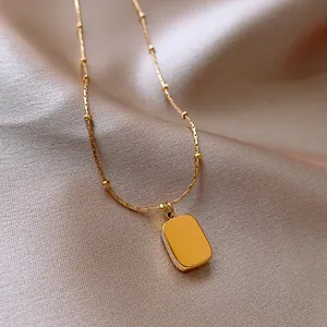 Macro view of polished gold rectangular pendant on elegant stainless steel satellite chain.