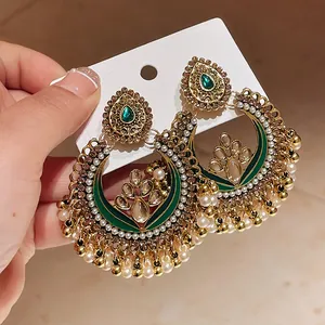 Close-up of ornate ethnic drop earrings with green enamel inlay and white pearls