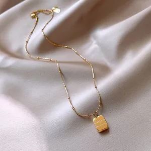 Close-up view of a gold-plated stainless steel necklace with engraved charm pendant on satin