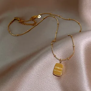 Close-up of a gold-toned stainless steel necklace with an engraved rectangular pendant.