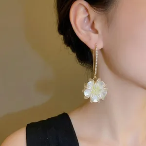 Elegant gold hoop earrings with sparkling rhinestones and a white floral charm on model
