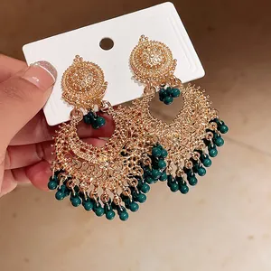 Detailed close-up view of vintage ethnic gold earrings with deep green bead tassels on card