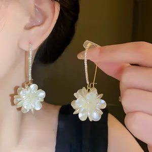 Detail view of elegant gold ear hook earrings with sparkling rhinestones and white floral charm